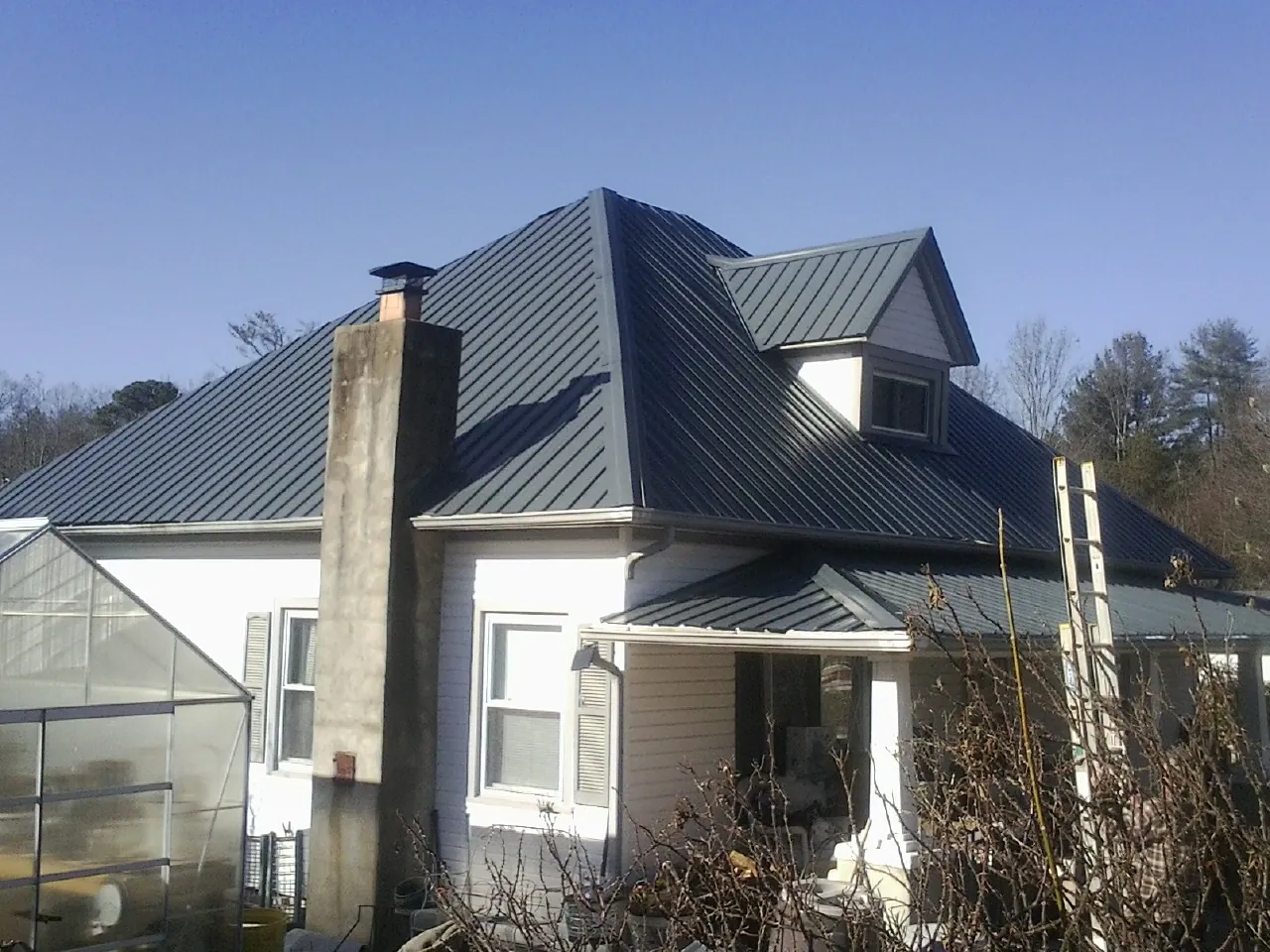 Dark blue standing seam metal roof on a white farmhouse with dormer — Slate & Tile Roof Repair by Roofing Brothers in Burnham