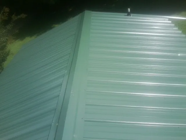 New green metal panels meeting at the ridge of a roof — Flat Roof Repair work by our crew in Burnham