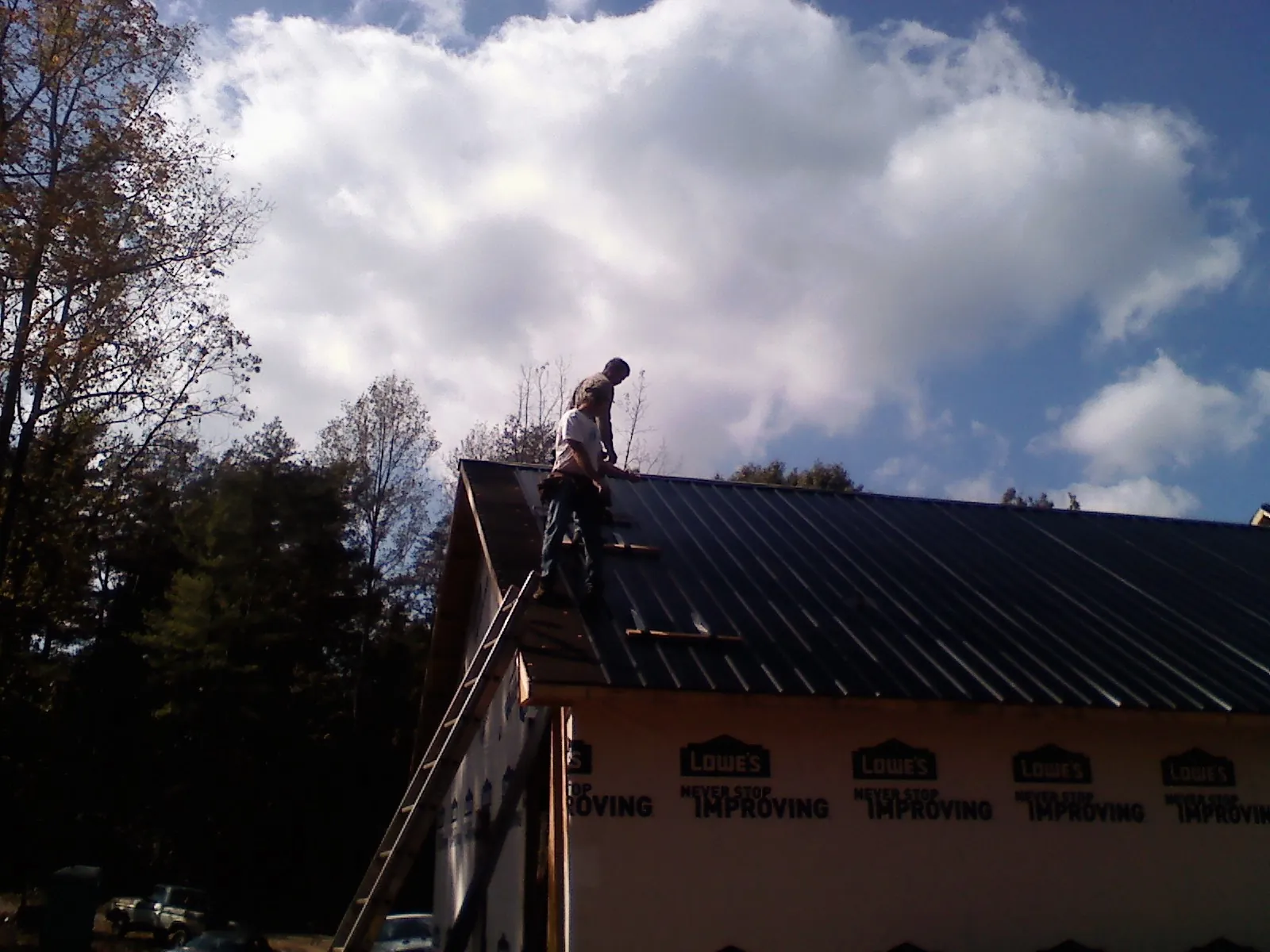 Roofer fastening dark metal panels high against a cloudy sky, from a Roof Inspection job in Burnham