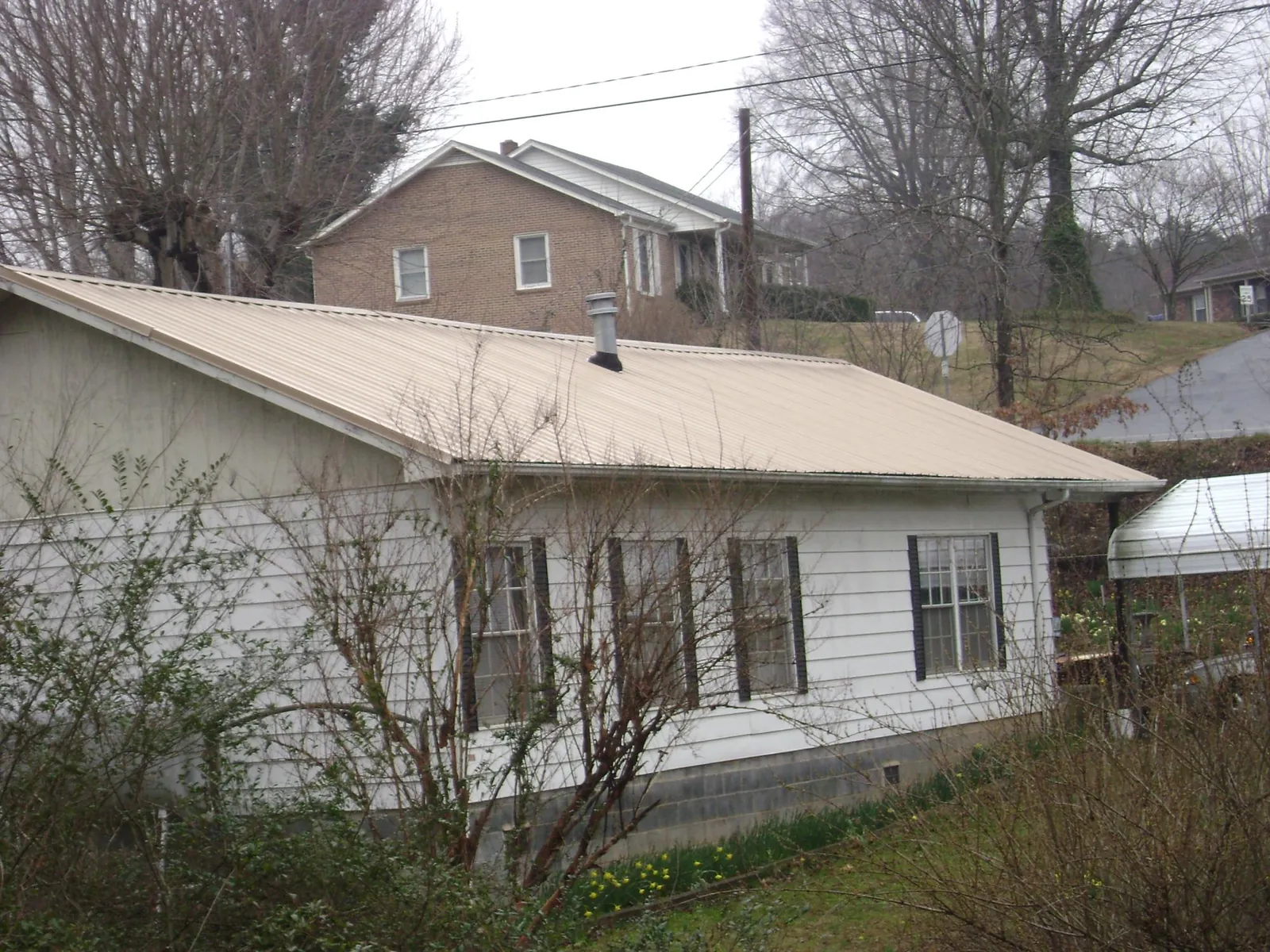 Tan metal roof on a white sided house set into a hillside — Commercial Roofing by Roofing Brothers in Burnham